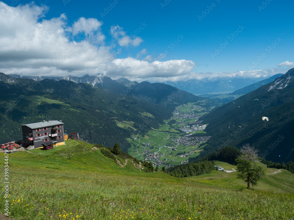 View over green Stubai valley and Neustift im Stubaital village with Elferhutte, grass meadow, moutain peaks and kites. Tirol Alps, Austria, Summer blue sky, white clouds