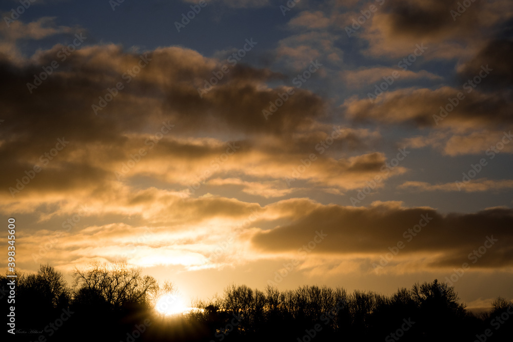 sunrise peeping above the treeline, blue sky and illuminated clouds