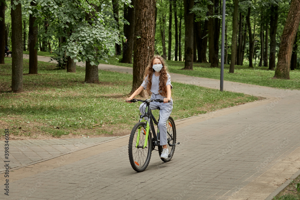 A beautiful girl with long hair rides a Bicycle in the Park in the summer on a tiled path. Outdoor activity.