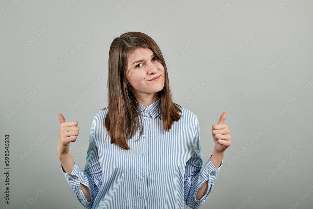 Showing thumbs up, like sign Positive something good has happened finger gesture for fine result well done. Young attractive woman, dressed blue shirt with brown eyes, brunette hair, grey background Showing thumbs up, like sign Positive something good has happened finger gesture for fine result well done. Young attractive woman, dressed blue shirt with brown eyes, brunette hair, grey background