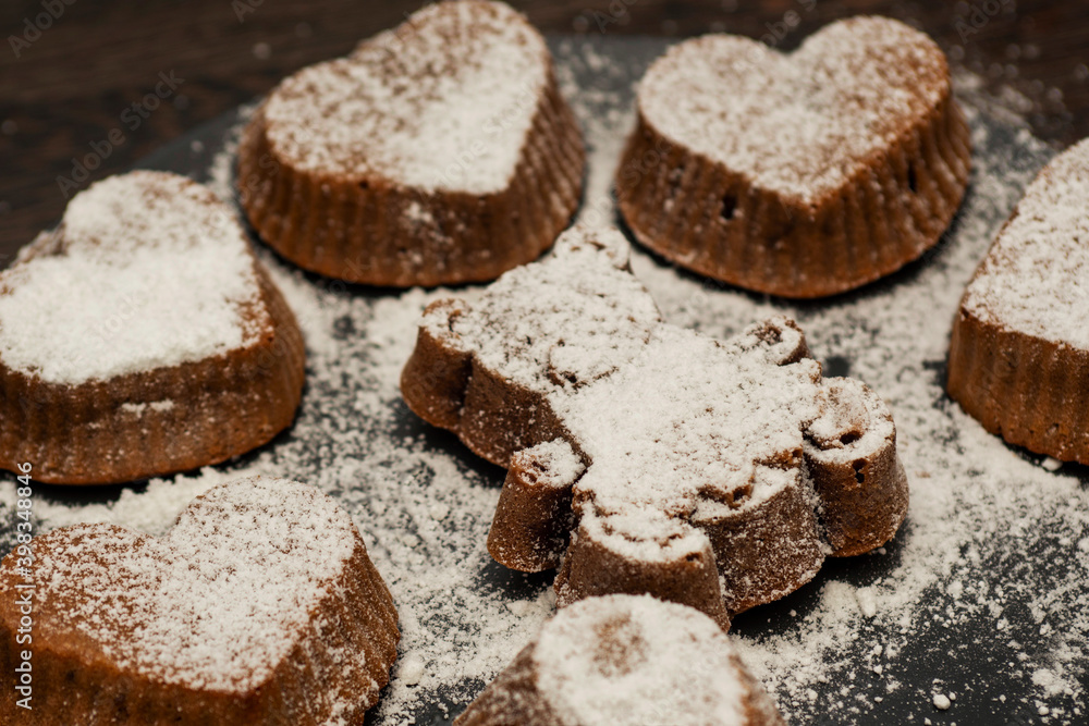 Delicious chocolate muffins or cupcakes in powdered sugar on black plate on dark wooden background. Homemade bakery Delicious chocolate muffins or cupcakes in powdered sugar on black plate on dark wooden background. Homemade bakery