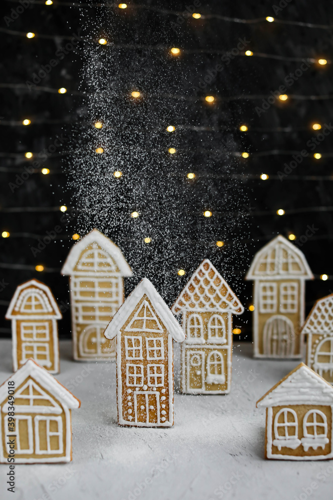 Gingerbread houses on the background of garland lights. New Year's traditional treats. Glazed Christmas cookies.