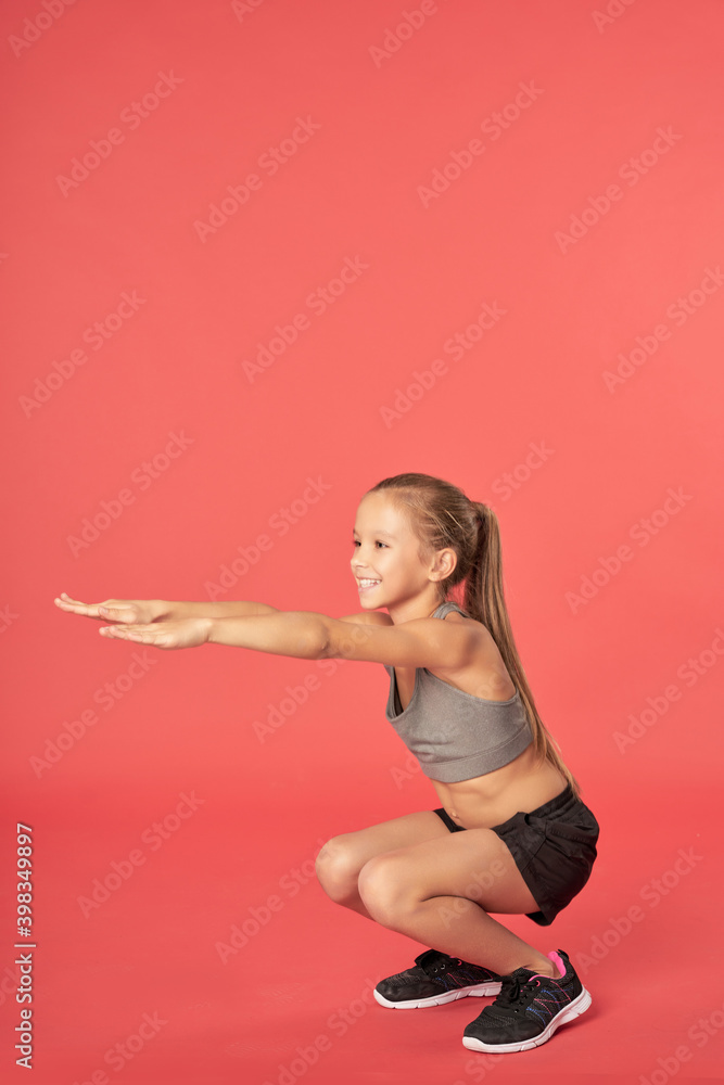 Cheerful female child in sportswear doing squats