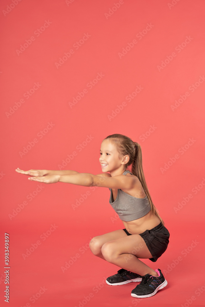 Cheerful female child in sportswear doing squats Cheerful female child in sportswear doing squats