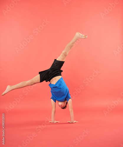 Fotografie, Obraz Sporty boy doing handstand exercise against red background