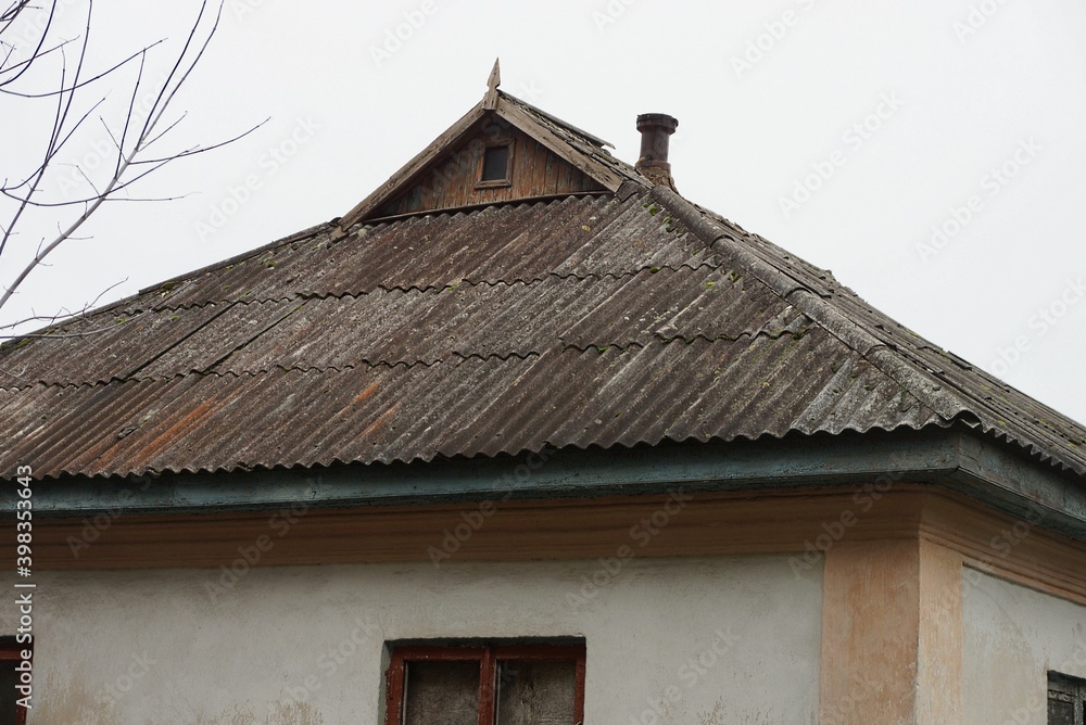 part of an old rural house under a gray slate roof on the street against the sky