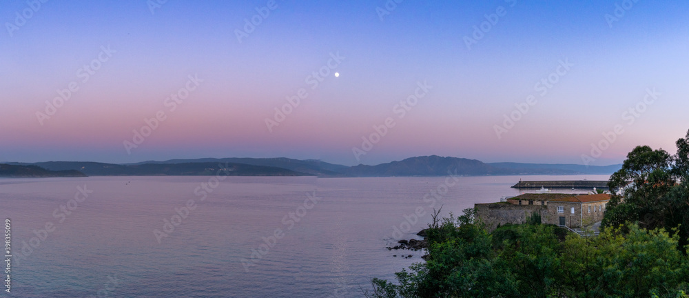 panorama view of the coast of Galicia and Fisterra with harbor at sunset under a full moon