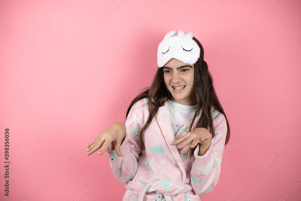 Pretty girl wearing pajamas and sleep mask over pink background disgusted expression, displeased and fearful doing disgust face because aversion reaction Pretty girl wearing pajamas and sleep mask over pink background disgusted expression, displeased and fearful doing disgust face because aversion reaction