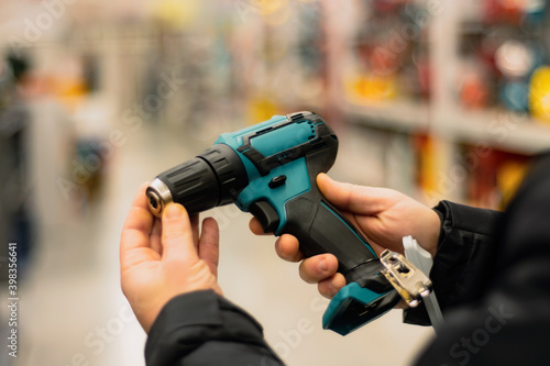 Man holds in his hands a green cordless screwdriver for repair work on the background of showcases in a hardware store.