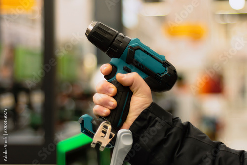 Man holds in his hands a green cordless screwdriver for repair work on the background of showcases in a hardware store.