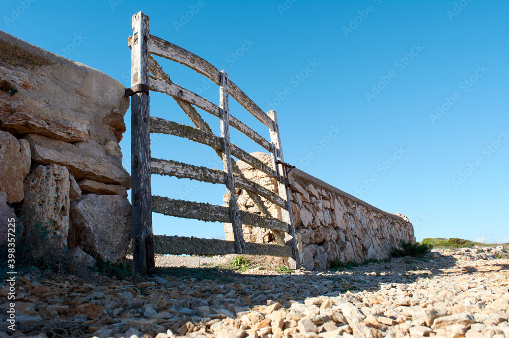 view from the ground, of typical wooden door, with lichens, in stone wall next to the road, with beautiful blue sky over Mediterranean forest, mallorca spain view from the ground, of typical wooden door, with lichens, in stone wall next to the road, with beautiful blue sky over Mediterranean forest, mallorca spain