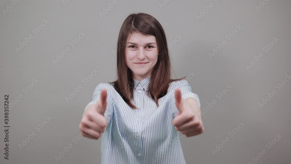 Showing thumbs up, like sign Positive something good has happened finger gesture for fine result well done. Young attractive woman, dressed blue shirt with brown eyes, brunette hair, grey background Showing thumbs up, like sign Positive something good has happened finger gesture for fine result well done. Young attractive woman, dressed blue shirt with brown eyes, brunette hair, grey background
