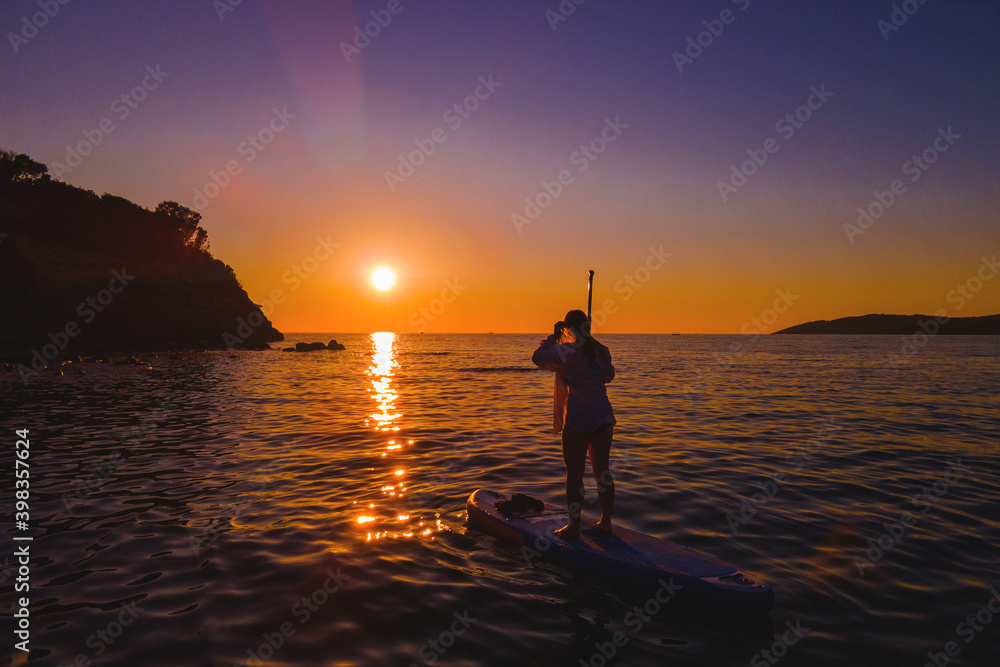 Silhouette of a woman on stand up paddle board against the backdrop of a beautiful sunset