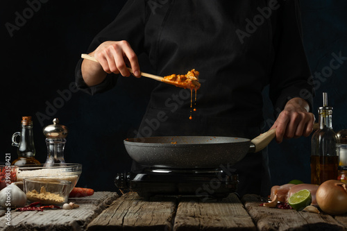 Chef testing hot frying chicken fillet with spices. Backstage of cooking traditional Indian chicken curry on dark blue background. Frozen motion. Concept cooking process. Frozen motion.