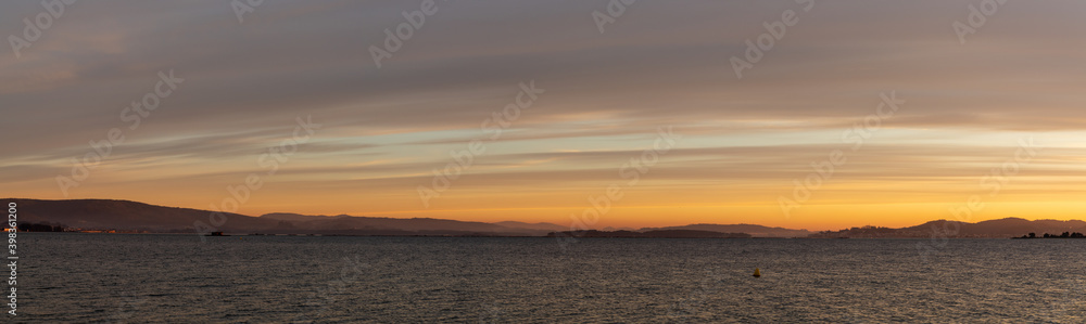 banner panorama of sunset over a calm ocean with hills and mountains in the background
