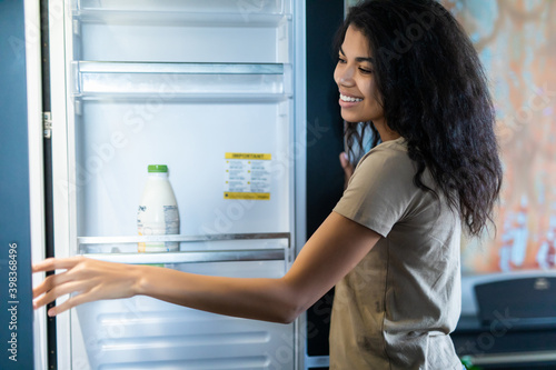 Young pretty afro woman open fridge in the kitchen