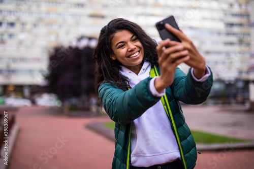 Young african woman student taking selfie on her smartphone outdoors on autumn street