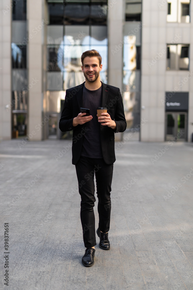 Confident young businessman using cell phone and drinking coffee in the city