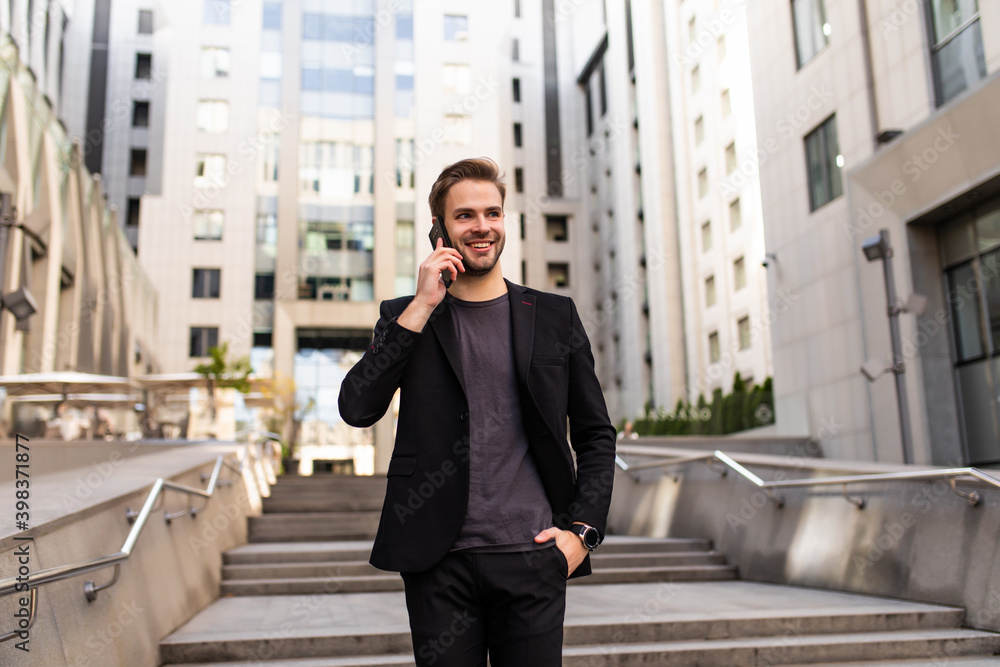 Portrait of employee man dressed in formal suit walking outside glass building and talking on mobile phone Portrait of employee man dressed in formal suit walking outside glass building and talking on mobile phone