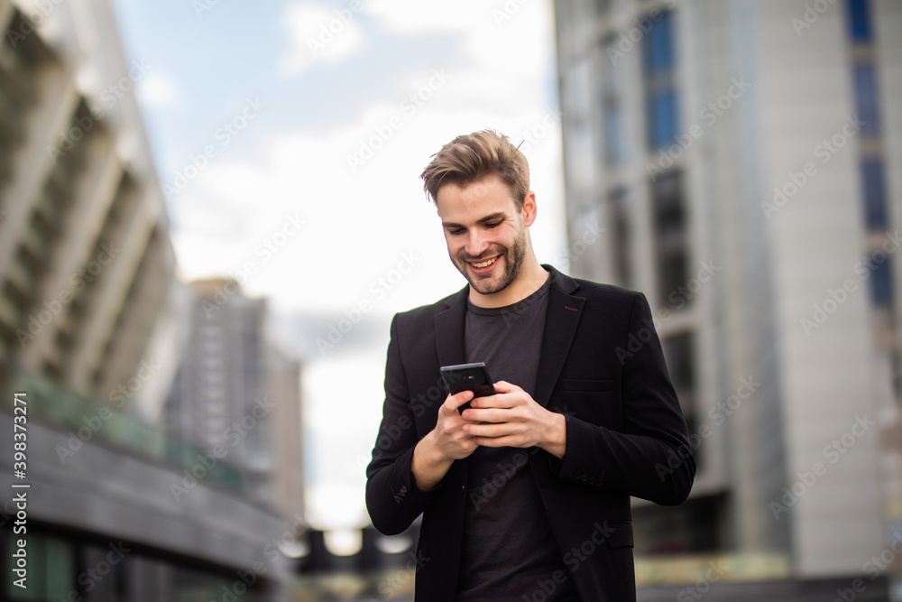 Young businessman is walking writing a message on his mobile phone. Skyline on a background Young businessman is walking writing a message on his mobile phone. Skyline on a background
