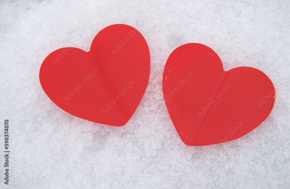 Fototapeta premium Two beautiful romantic red hearts together on a white snowy background. The concept of love and Valentine's Day
