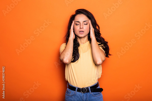 Whats happening. Stressful displeased beautiful woman, keeps hands on head, forgets something important, has displeased sad expression, does not know what to do, isolated on orange background