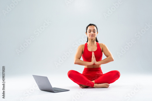 Young pretty woman sitting in yoga pose lotus with laptop isolated on white background