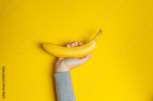 Female hand in gray clothes holding one banana on yellow background. Creative banner with two colors of the year 2021 - Illuminating and Ultimate Gray. photo