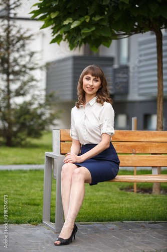 Young woman weared in classic business suit on background of a City park. Business style girl in Summer City on background of new park near a building. Street style Modern strict urban girl.