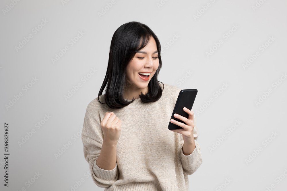 Happy young asian woman looking at screen of smartphone standing on isolated white background. She very happy. Happy young asian woman looking at screen of smartphone standing on isolated white background. She very happy.