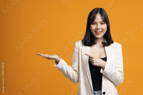 Attractive Beautiful asian woman open hands palm up holding something. Sexy happy female in suit on isolated yellow background. © Chanakon