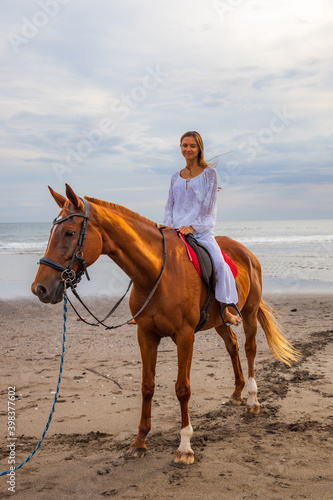 Beautiful caucasian woman riding horse on the beach. Female wearing white clothes. Copy space. Sunset time on the beach. Outdoor activities.