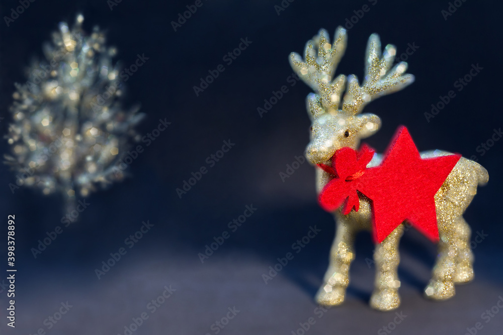 Golden, shiny reindeer figurine with a christmas tree on a dark background. Christmas background/card, gift card, red star - pendant/tag. Copy space.