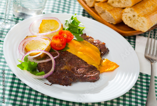 Well-done beef steak with cheese and baked potatoes at plate with greens