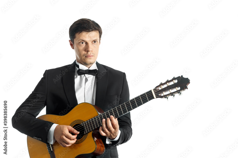 young man in black classic suit with bow tie posing with classical guitar in studio on white background.