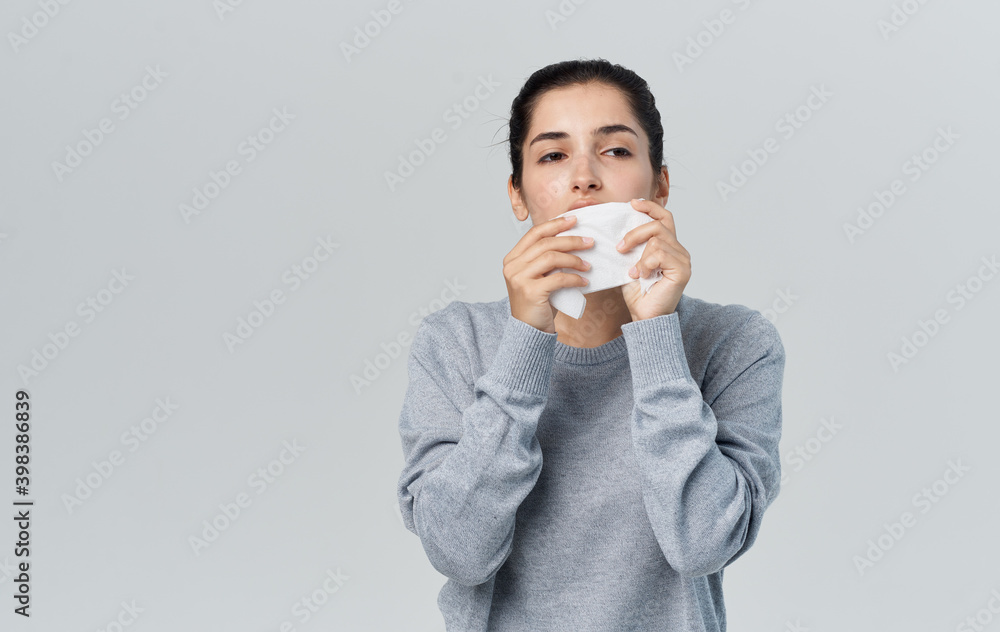 Sick woman blows her nose with napkin on gray background and warm sweater cropped view Sick woman blows her nose with napkin on gray background and warm sweater cropped view