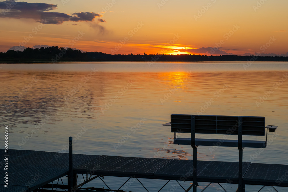 Evening scene at a lake in Bemidji, Minnesota, with an empty dock bench, and a few ripples on the reflective water.