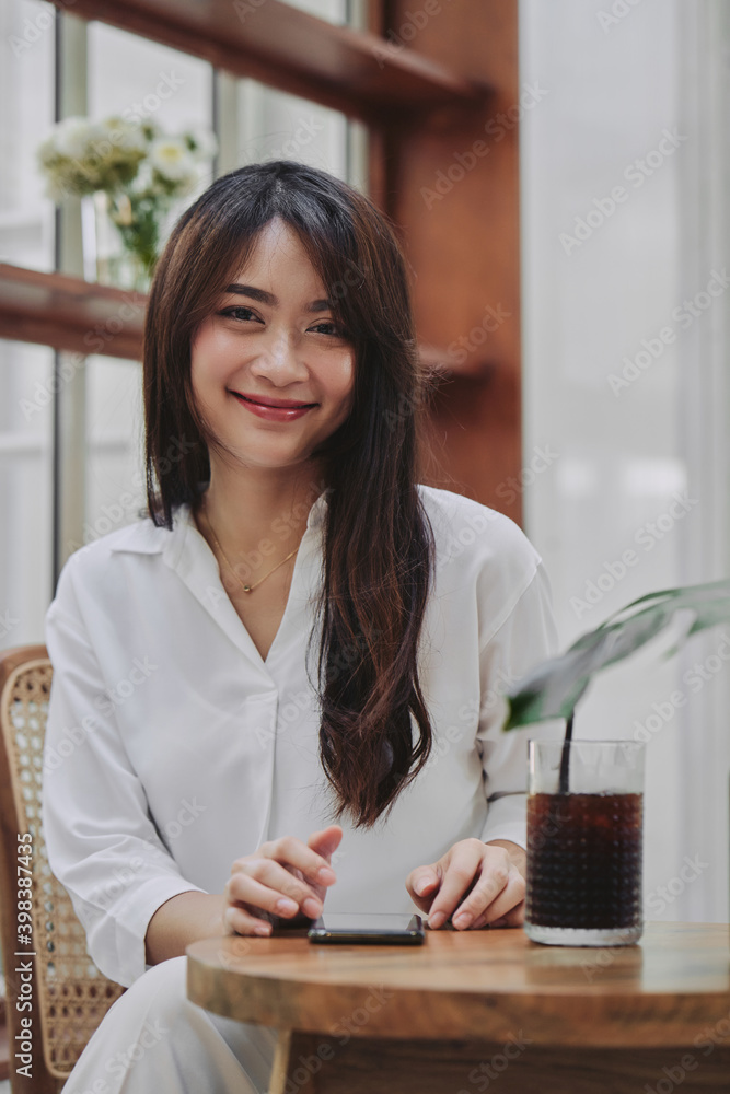 happy asian young woman drinking iced coffee in coffee hop while using her phone