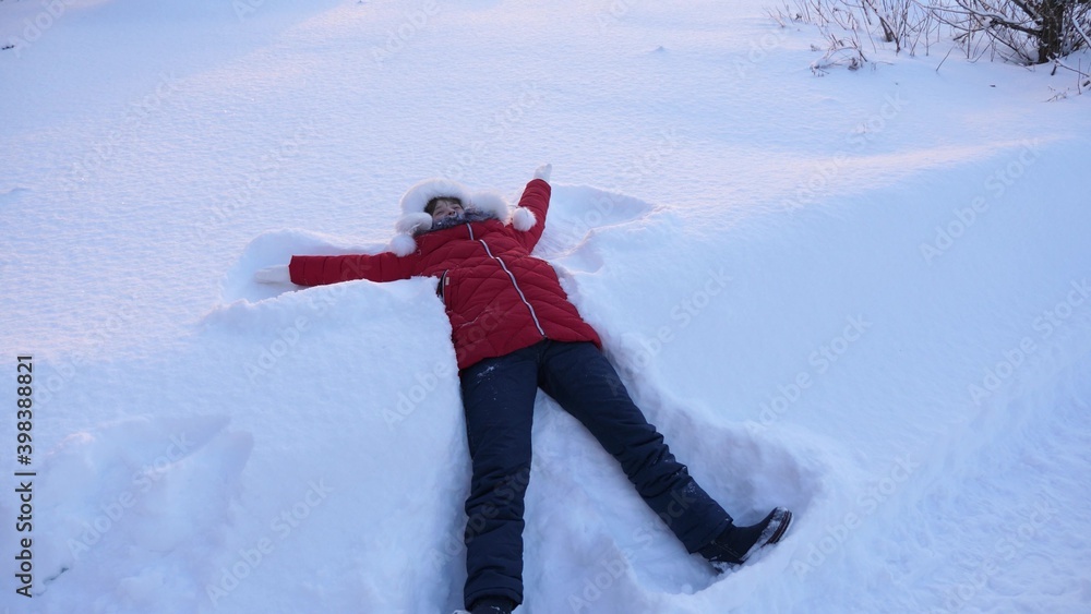 Happy little girl lying in snow creating a snow angel, moving arms and legs, lying on her back. A child is playing in a winter park in snow on Christmas holidays. Healthy little girl. Merry Christmas