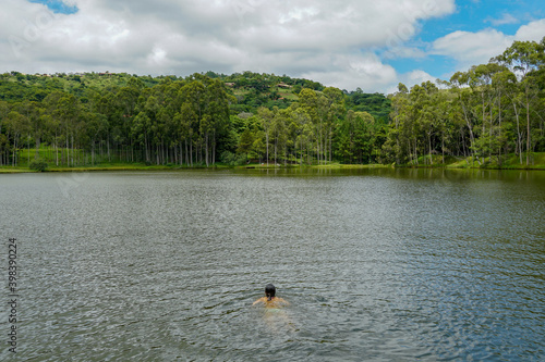 Young lady swimming in a small lake surrounded by green land and wood forest.. Monte Alegre Do Sul, Brazil. 