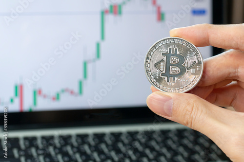 Hand holding golden Bitcoin virtual money. Hand holding Bitcoin (New virtual money) coin over us dollars close up selective focus. Bitcoin exchange financial chart with man holding bitcoin.