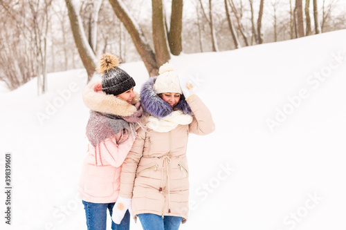 Two girls play snowballs in the winter in the forest. Sisters in a warm dress have fun with snow in winter