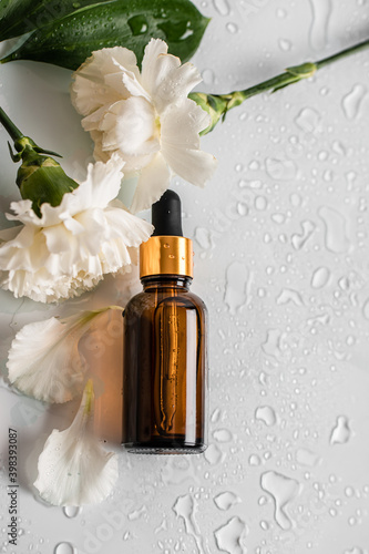 Glass brown serum bottle with pipette for skin care with flowers and drops isolated on white background. Health and beauty concept. Copy space