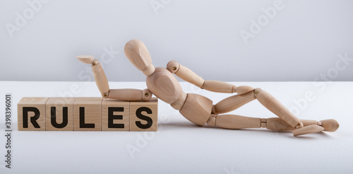 The wooden man lies near the wooden cubes with the text RULES. Business concept.