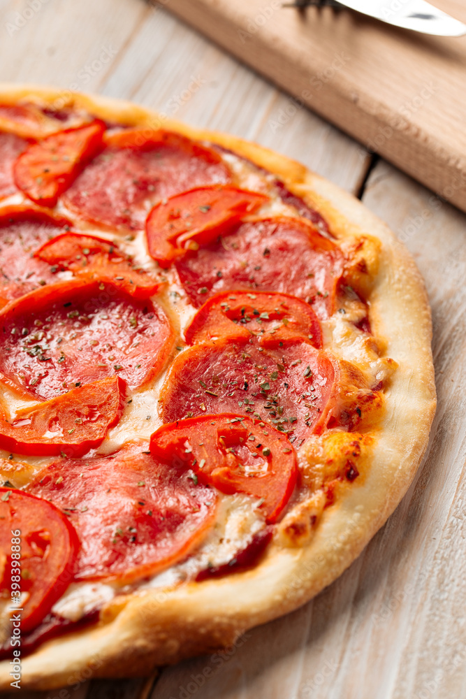 Closeup on ham pizza with tomato with dried herbs on the wooden table