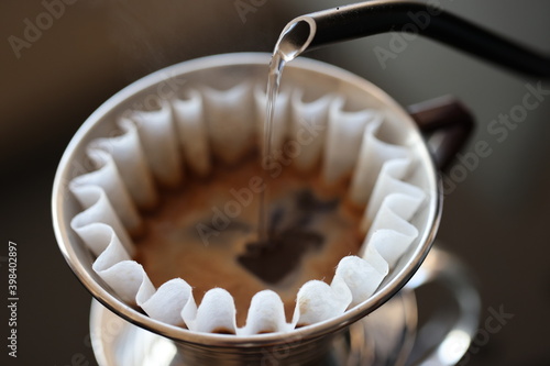 Barista making coffee with a pour over coffee maker in a dripper and pouring hot water from a black pot on a macro scale