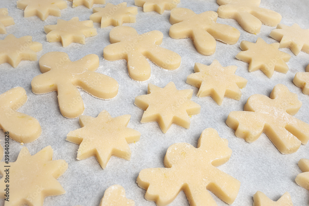 Many cookies on baking sheet. Diagonal rows of short bread cookies dough in different shapes such as: star, gingerbread man and angel. Traditional Christmas baking, home made dough. Selective focus.
