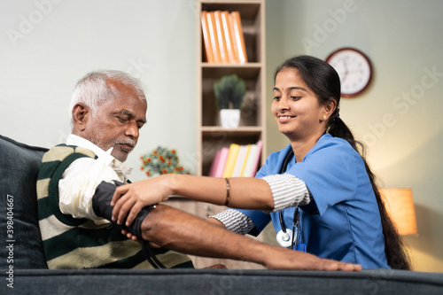 Nurse of doctor busy in setting up BP or blood pressure medical equipment to senior man at home of check up at home - concept of routine home help check. photo