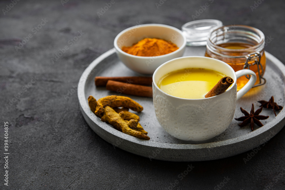 Yellow turmeric latte drink. Golden milk with cinnamon, turmeric, ginger and honey over black concrete background. Yellow turmeric latte drink. Golden milk with cinnamon, turmeric, ginger and honey over black concrete background.