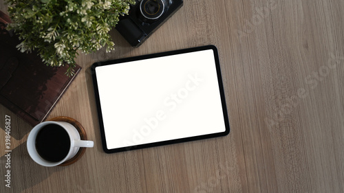 Top view of contemporary workplace with coffee cup, plant, book and tablet on wooden desk. Blank screen for product montage.